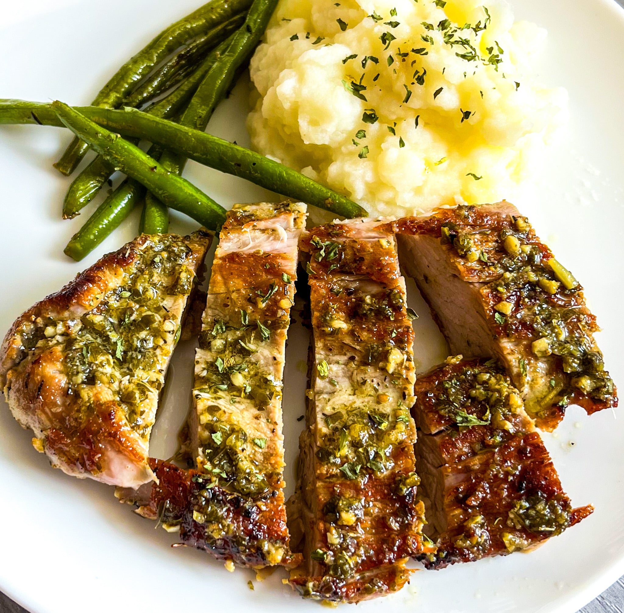 close up of garlic and herb pork tenderloin served with mashed potatoes and green beans