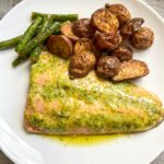 pesto butter salmon on a white plate served with roasted potatoes and green beans