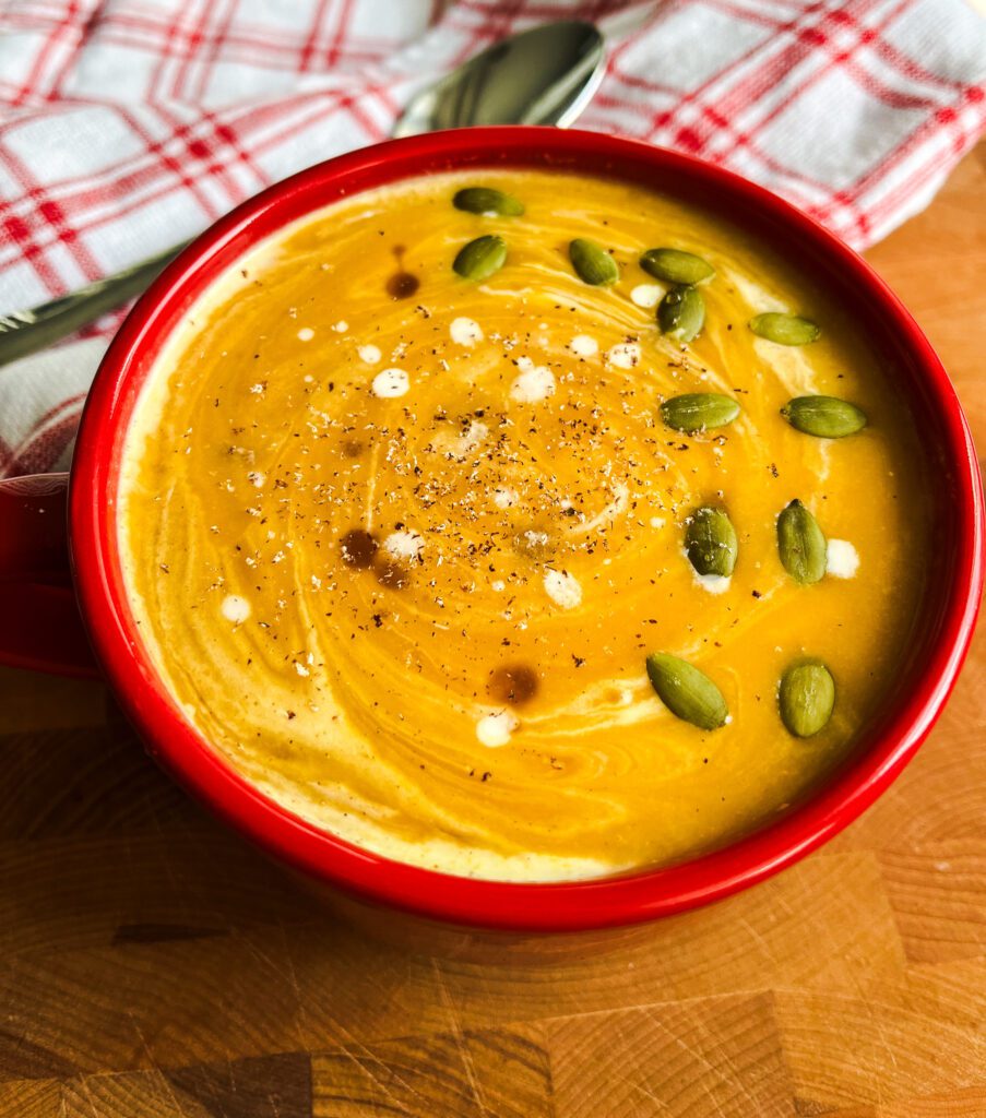 butternut squash soup garnished with pumpkin seeds and grated nutmeg in a red bowl