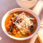 minestrone soup in a white bowl topped with shredded parmesan cheese