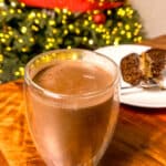 Super Creamy Brazilian Hot Chocolate served in a clear glass with a Christmas tree and chocolate cake in the background.