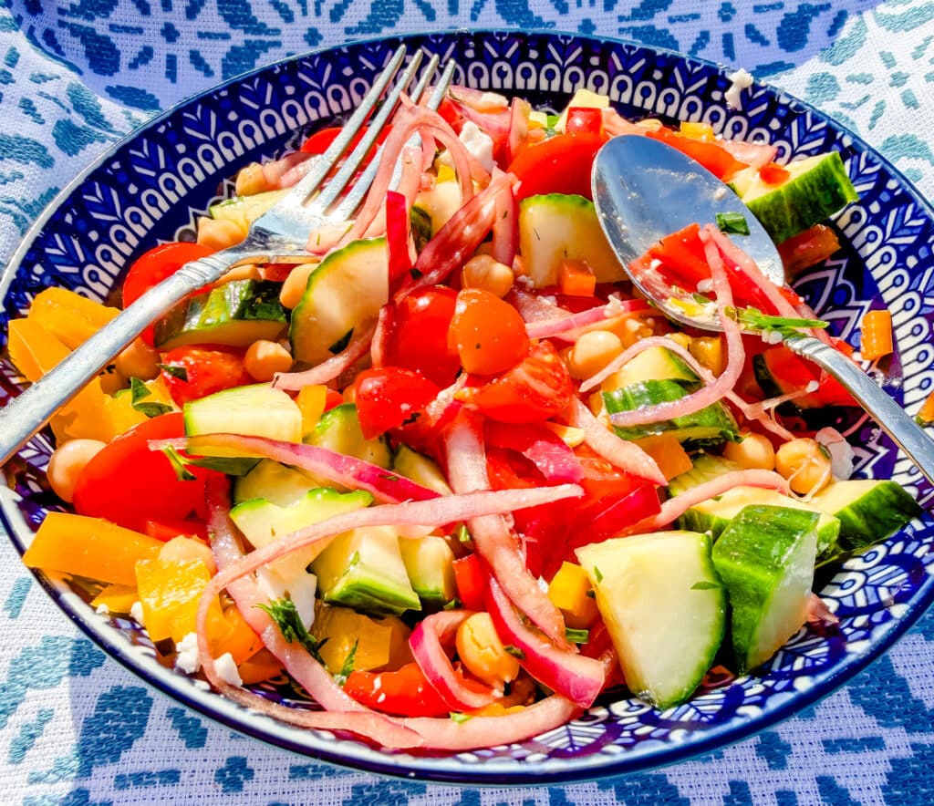 greek salad with pickled red onions on a bright blue plate with fork and a spoon