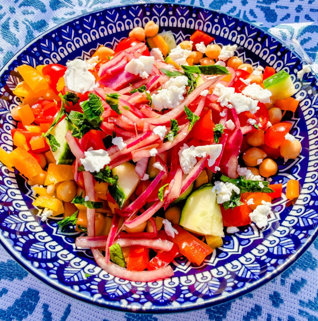 greek salad with pickled red onions on a bright blue plate view from side