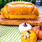 loaf of pumpkin bread on cutting board with decorative pumpkins near it