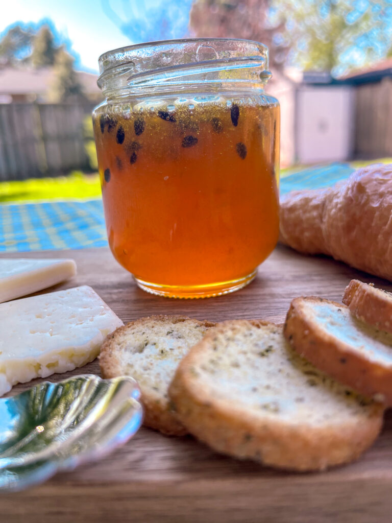Up-close shot of Homemade passion fruit jam on a rustic wooden board with croissant and cheese, on a green and white checkered tablecloth in sunlight with a soft shadow