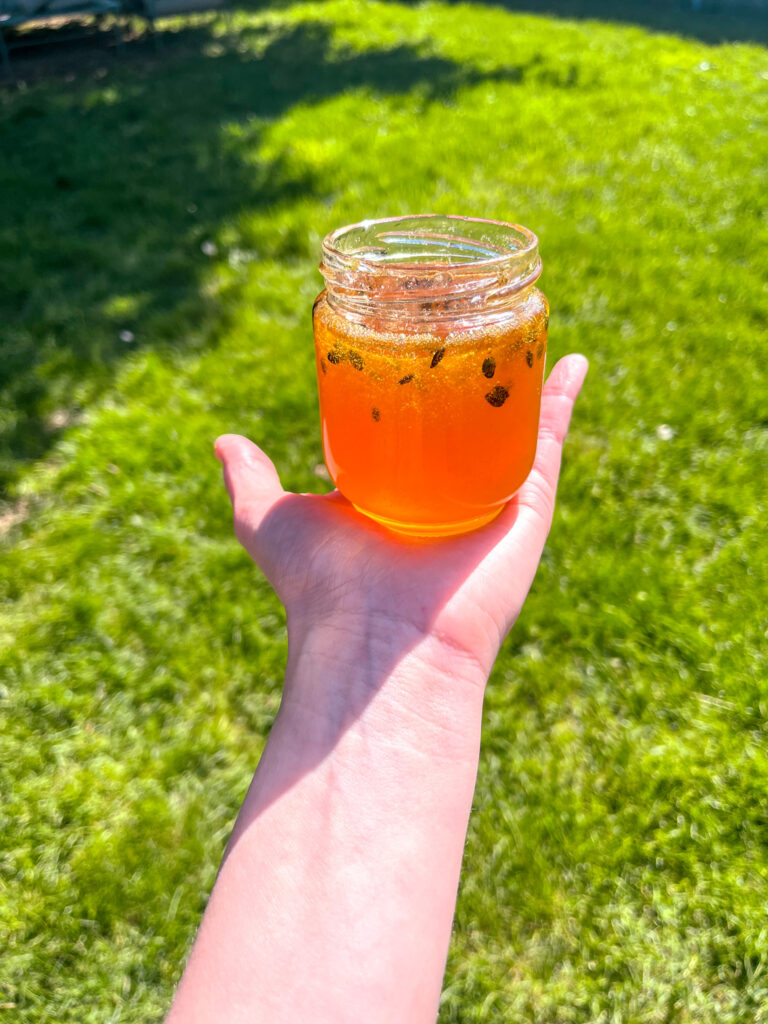 Hand holding a jar of homemade passion fruit jam over green grass in bright sunlight