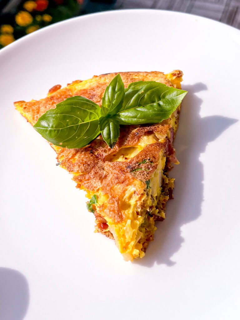 slice of potato omelette with basil on top on a white plate