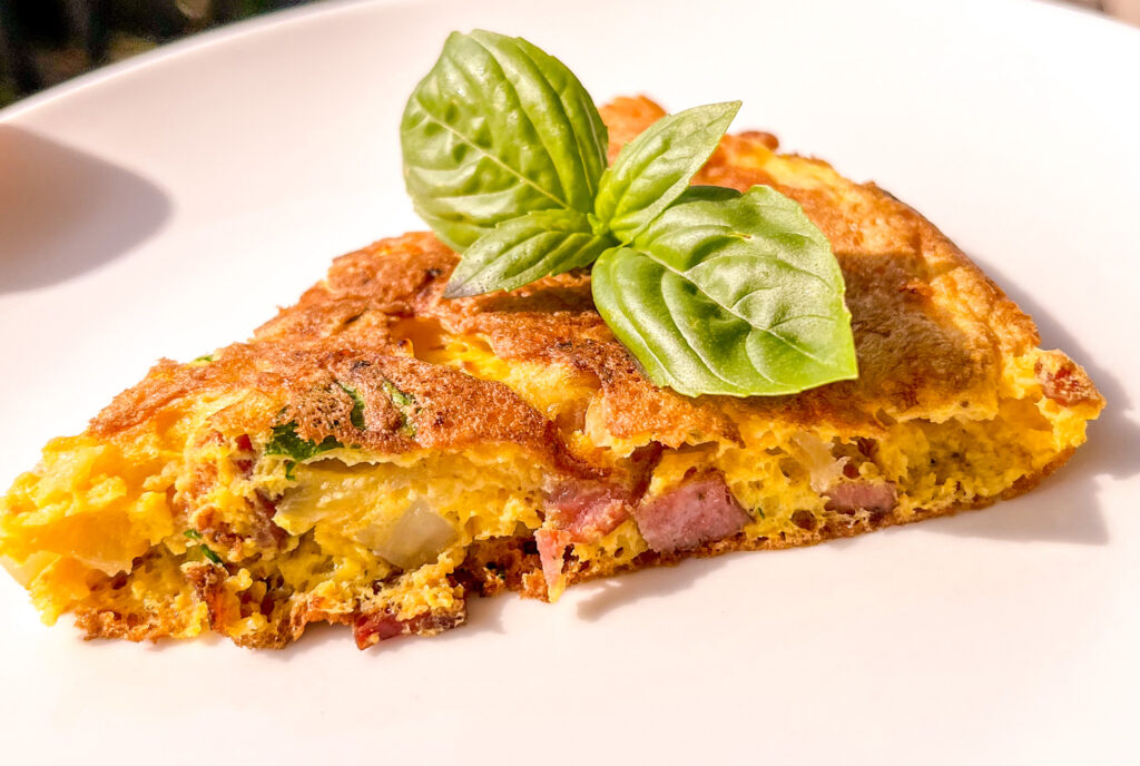 slice of potato omelette with basil on top on a white plate