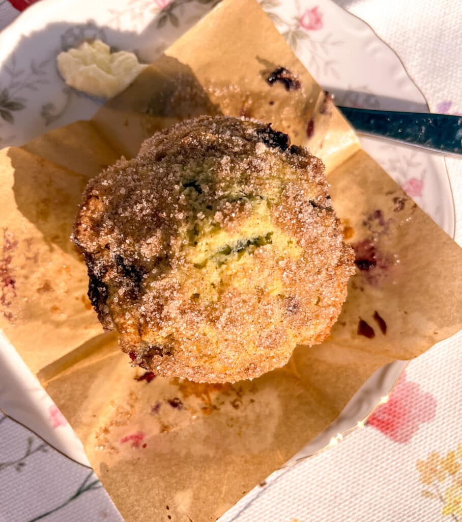 Bakery-style blueberry muffin in a tulip liner with butter knife nearby, ready to spread on the warm muffin