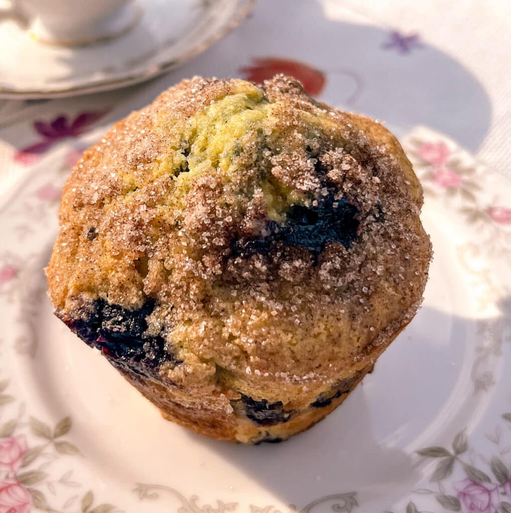 Easy and Fluffy Blueberry Muffins muffin on a china plate with pink flowers and a tea cup nearby.