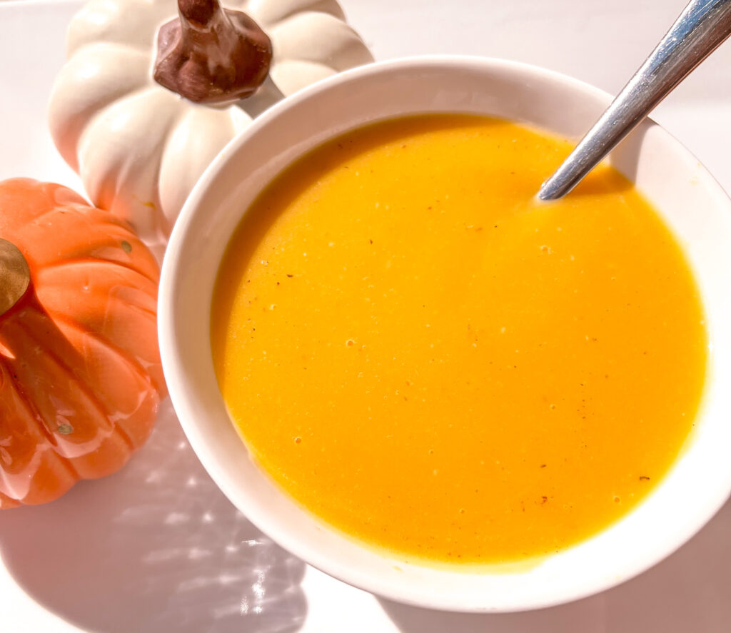 Easy Butternut Squash soup in a white bowl beside two decorative pumpkins