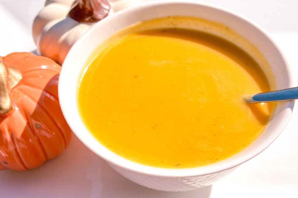 Easy Butternut Squash soup in a white bowl beside two decorative pumpkins