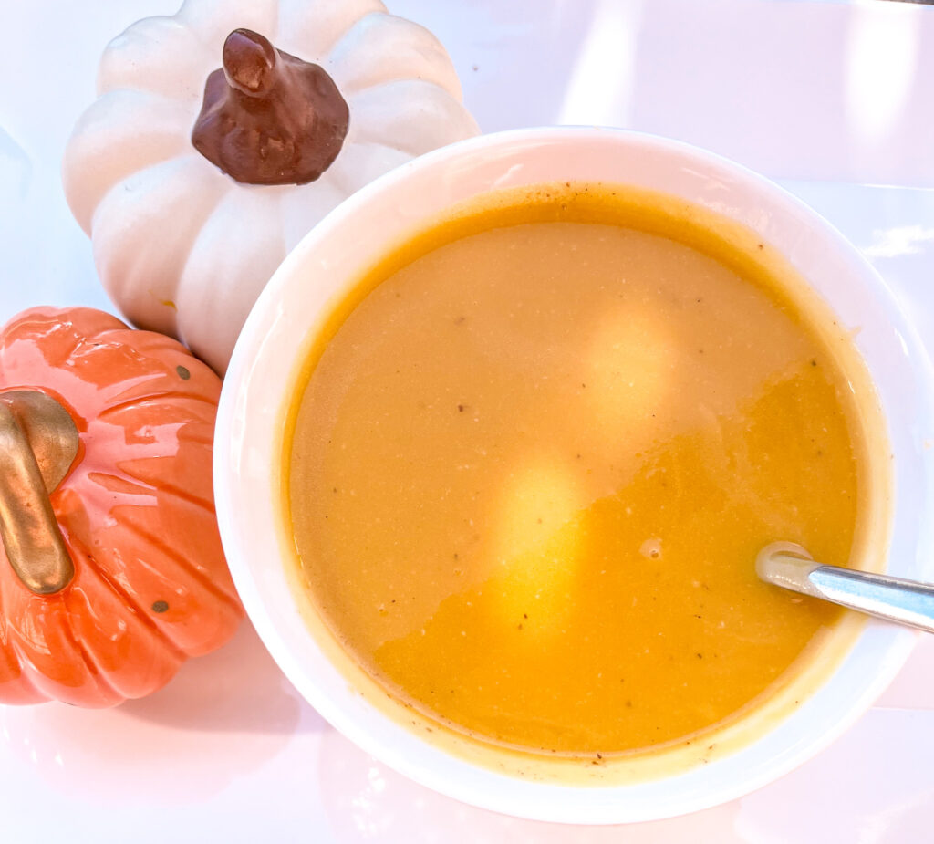 Easy Butternut Squash soup in a white bowl beside two decorative pumpkins