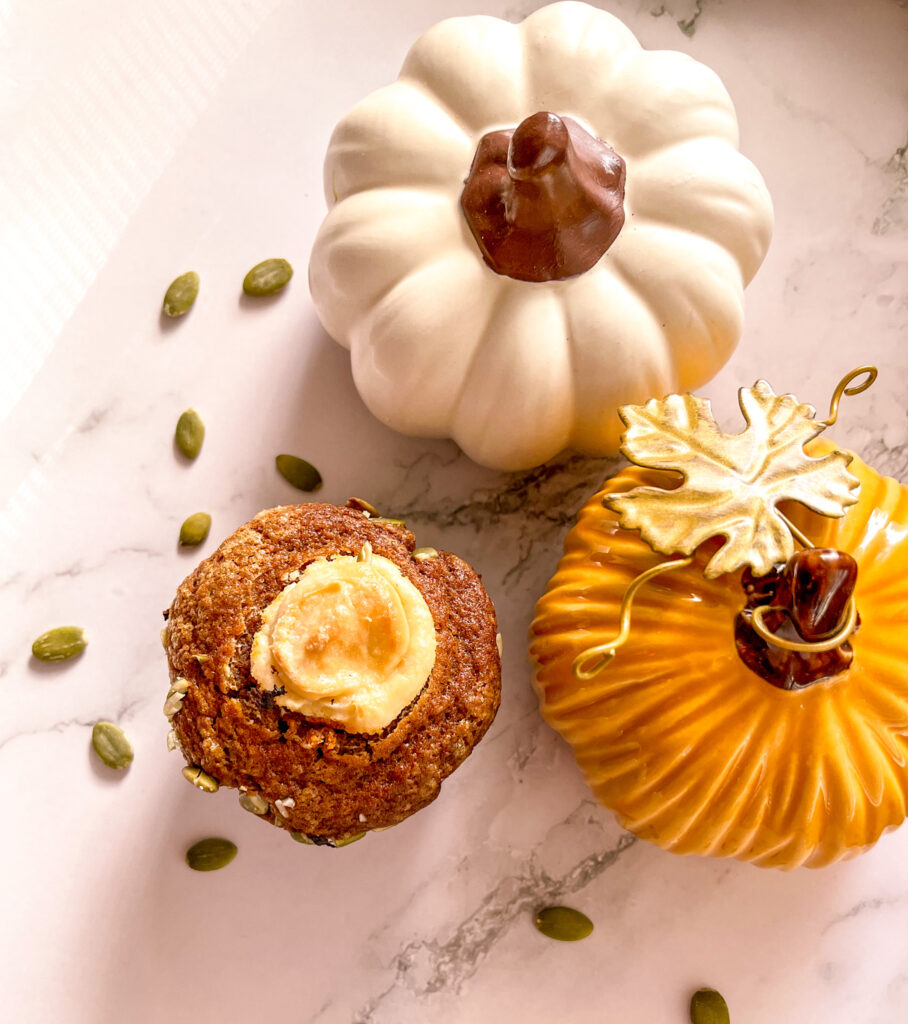 Pumpkin muffins with cream cheese filling beside white and yellow decorative pumpkins