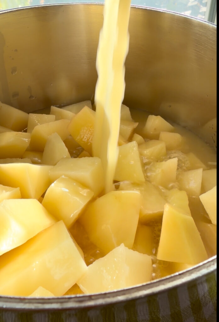 up close shot of broth pouring into a pot with chopped potatoes