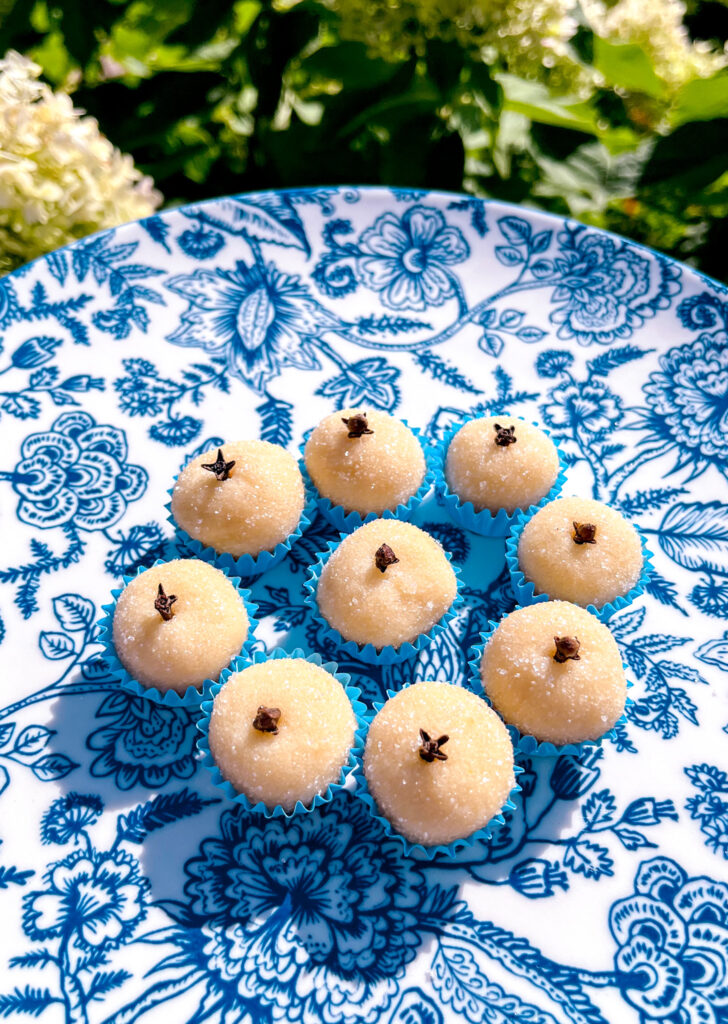 white brigadeiros in blue paper cups on a blue and white plate near garden