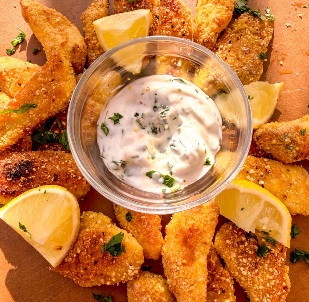 up close shot of crispy cornmeal tilapia arranged around sauce on a wooden cutting board