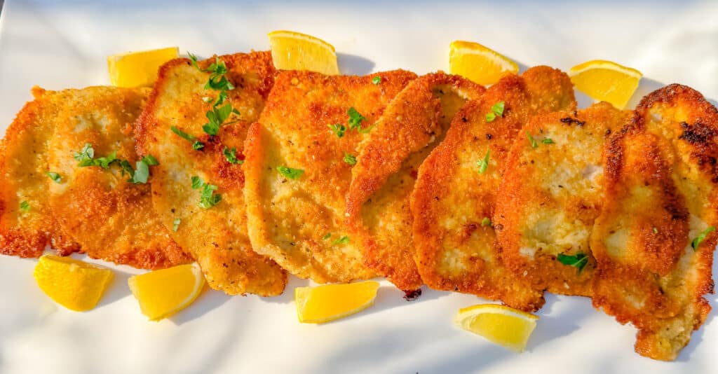 parmesan crusted pork chops on a white platter with lemons around it
