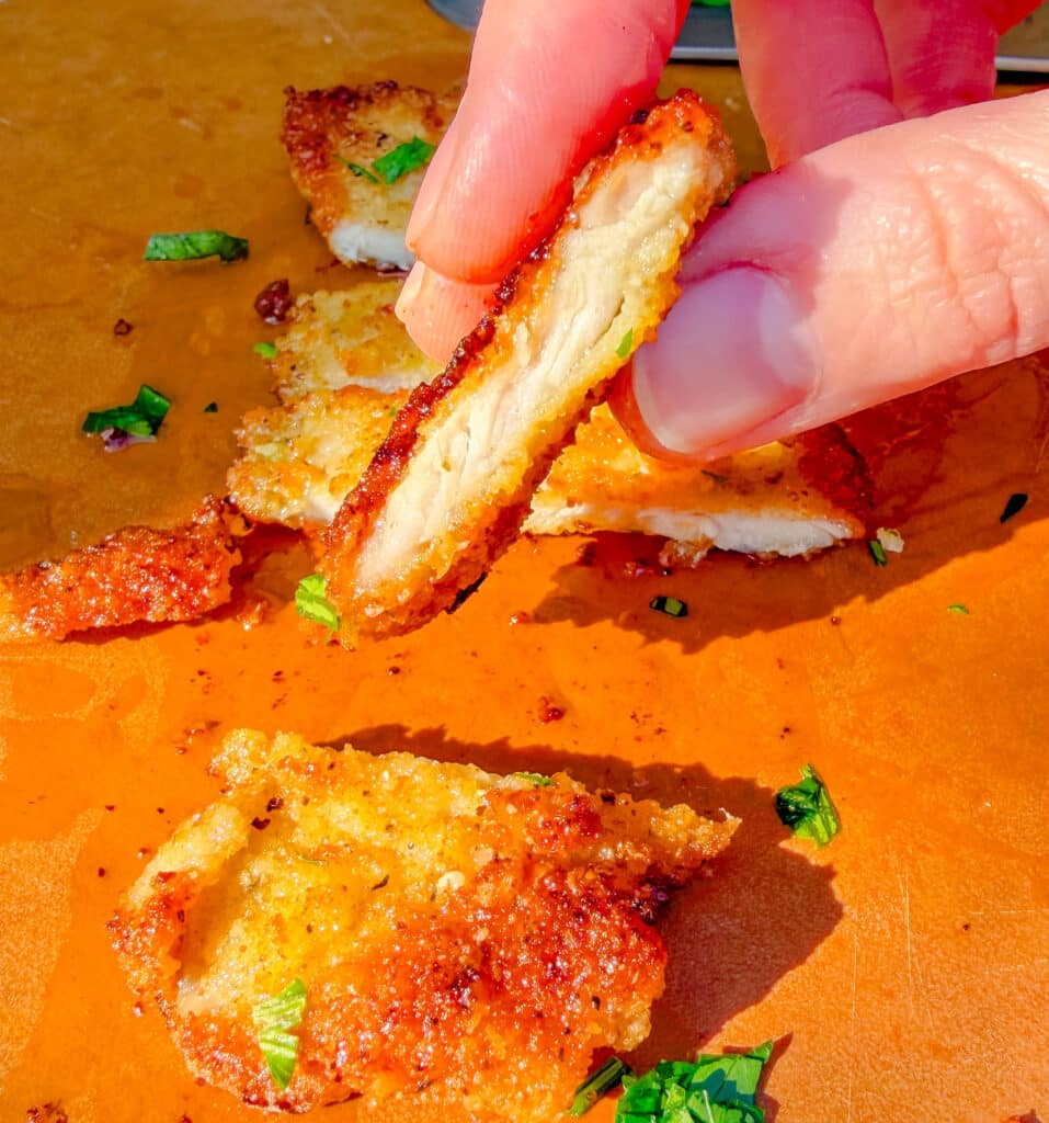 holding a slice of parmesan crusted pork chop