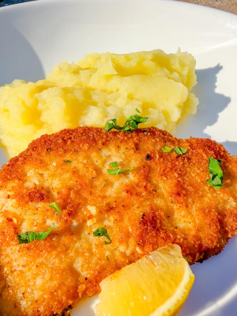 pork chop near lemon and mashed potatoes on a white plate