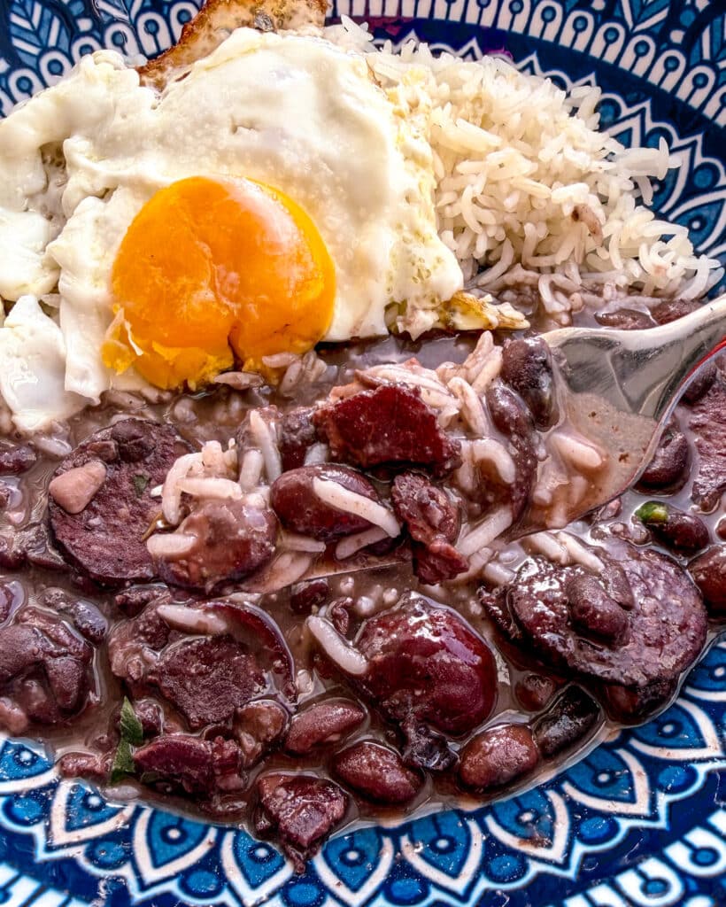 brazilian black beans with bacon in a colorful blue plate with an egg on top with the yolk pierced