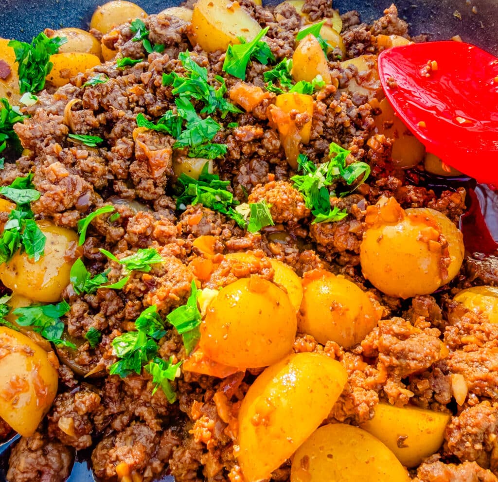 upclose ground beef and potatoes with lots of parsley on top spatula beside it on a skillet