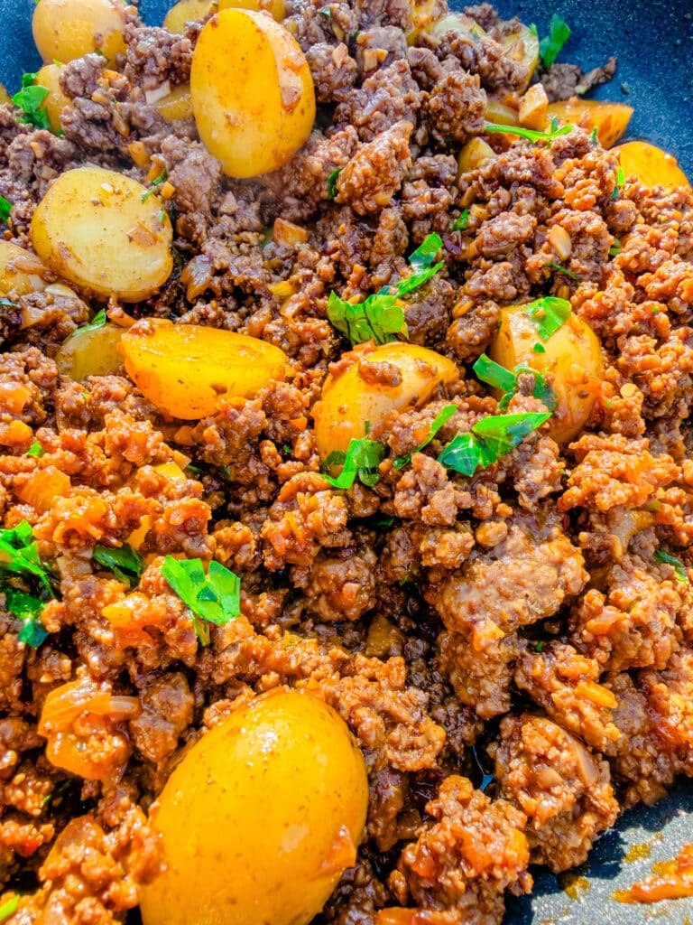 ground beef and potatoes with parsley on top spatula beside it on a skillet