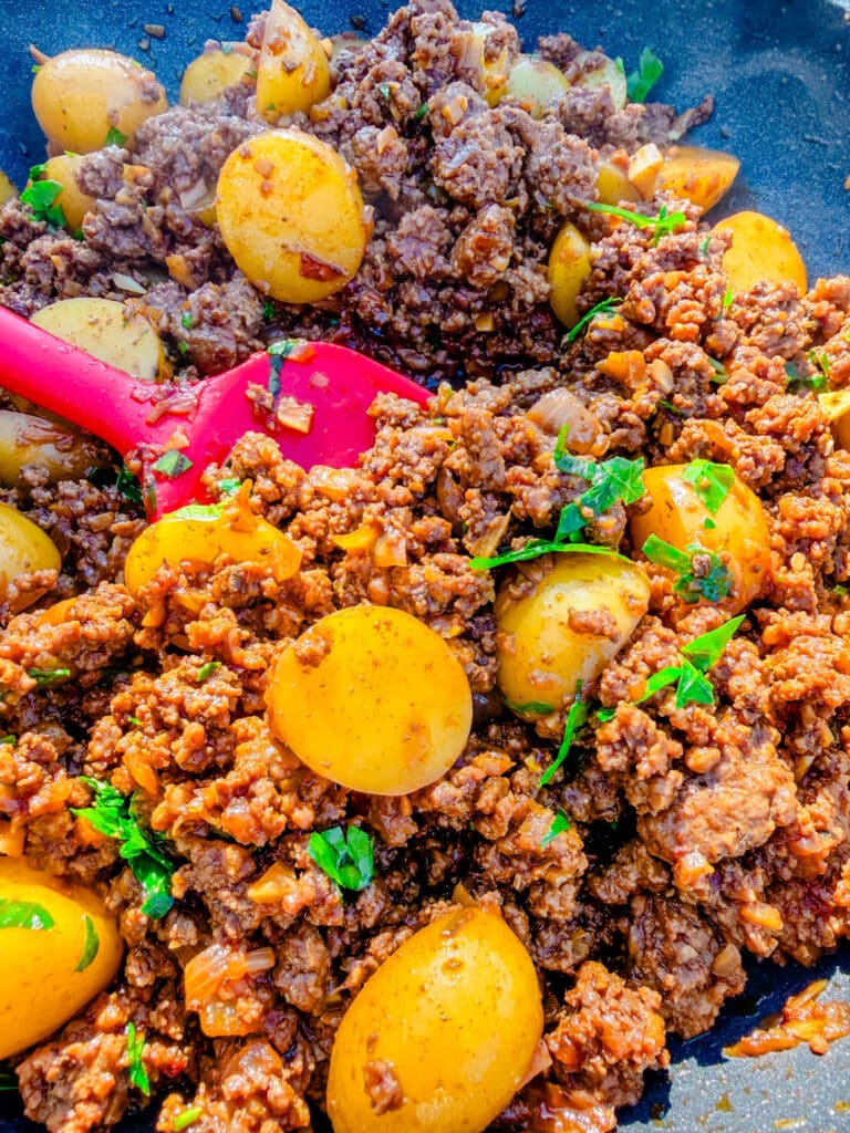 ground beef and potatoes with parsley on top spatula beside it on a skillet